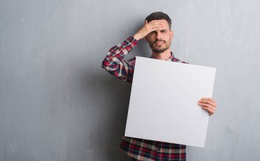 Genç yetişkin adam kafasına, el ile vurguladı afiş tutarak tuğla duvarın üzerinden şok utanç ve sürpriz suratla, öfkeli ve sinirli. Korku ve hata için üzgün.
