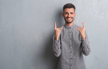 Genç yetişkin adam gri grunge rock simge elle yapıyor deli ifade ile bağırarak duvarın üzerinden ayakta. Müzik yıldızı. Ağır kavramı.