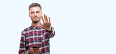 Genç yenilikçi yetişkin adam açık eliyle dur işareti ile ciddi ve kendine güvenen ifade, savunma jest yapıyor Smartphone holding
