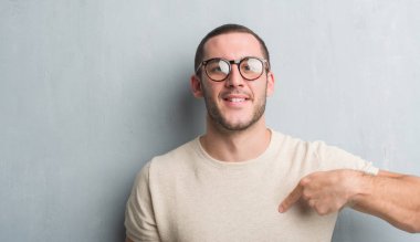 Sürpriz yüz işaret parmağı kendisine gri grunge duvarın üzerinden beyaz delikanlı