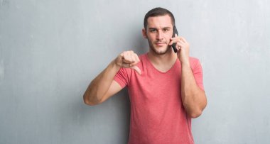 Kızgın yüz, eksi işareti aşağı antipati başparmak ile gösterilen, ret kavramı ile telefonda konuşurken gri grunge duvarın üzerinden beyaz delikanlı