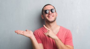 El ve parmak ile işaret çok mutlu güneş gözlüğü takıyor gri grunge duvarın üzerinden beyaz delikanlı