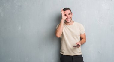 Gri grunge üzerinde beyaz delikanlı duvar manifatura mutlu yüz el parmaklarının arasından seyir göz üzerinde ok işaretiyle yapıyor gülümseyen ile smartphone kullanarak bir ileti