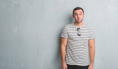 Komik surat ile yanakları şişirme gri grunge duvarın üzerinden Genç beyaz adam. Ağız ile hava, deli ifade şişirilmiş.