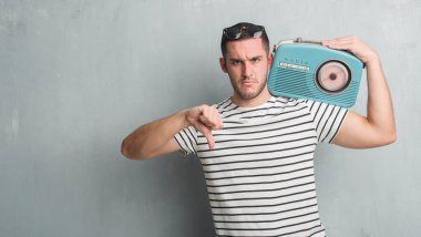Gri grunge Genç beyaz adam kızgın yüzü, eksi işareti aşağı antipati başparmak ile gösterilen, ret kavramı ile vintage radyo dinleme Müzik Duvar