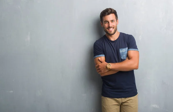 Handsome young man over grey grunge wall happy face smiling with crossed arms looking at the camera. Positive person.