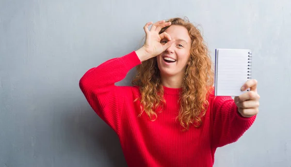 Unga Rödhårig Kvinna Över Grå Grunge Vägg Visar Tom Anteckningsbok — Stockfoto