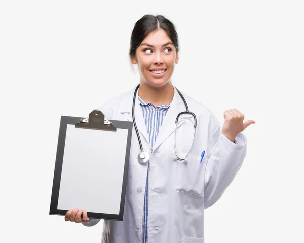 Young Hispanic Doctor Woman Holding Clipboard Pointing Showing Thumb Side — Stock Photo, Image