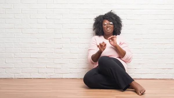 Young african american woman sitting on the floor at home disgusted expression, displeased and fearful doing disgust face because aversion reaction. With hands raised. Annoying concept.