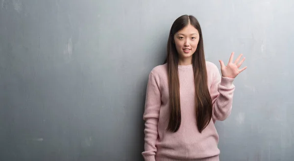 年轻的中国妇女在灰色墙壁显示和指向用手指五 而微笑自信和愉快 — 图库照片