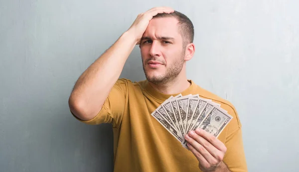 Young Caucasian Man Grey Grunge Wall Holding Dollars Stressed Hand — Stock Photo, Image