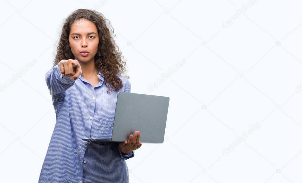 Young hispanic woman holding computer laptop pointing with finger to the camera and to you, hand sign, positive and confident gesture from the front