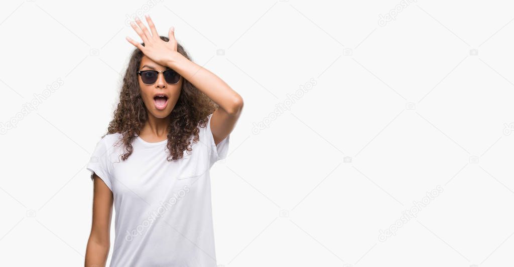 Young hispanic woman wearing sunglasses surprised with hand on head for mistake, remember error. Forgot, bad memory concept.