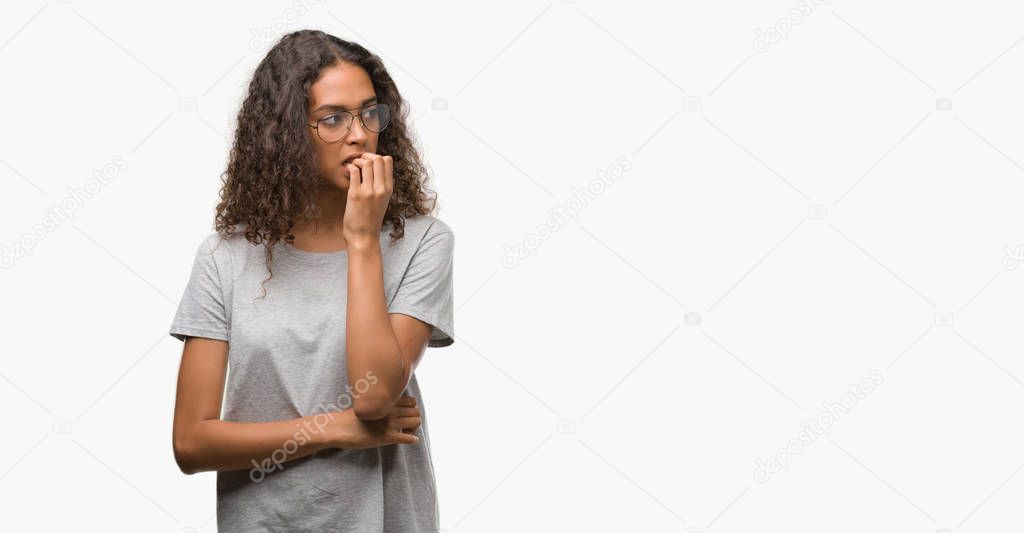 Beautiful young hispanic woman wearing glasses looking stressed and nervous with hands on mouth biting nails. Anxiety problem.