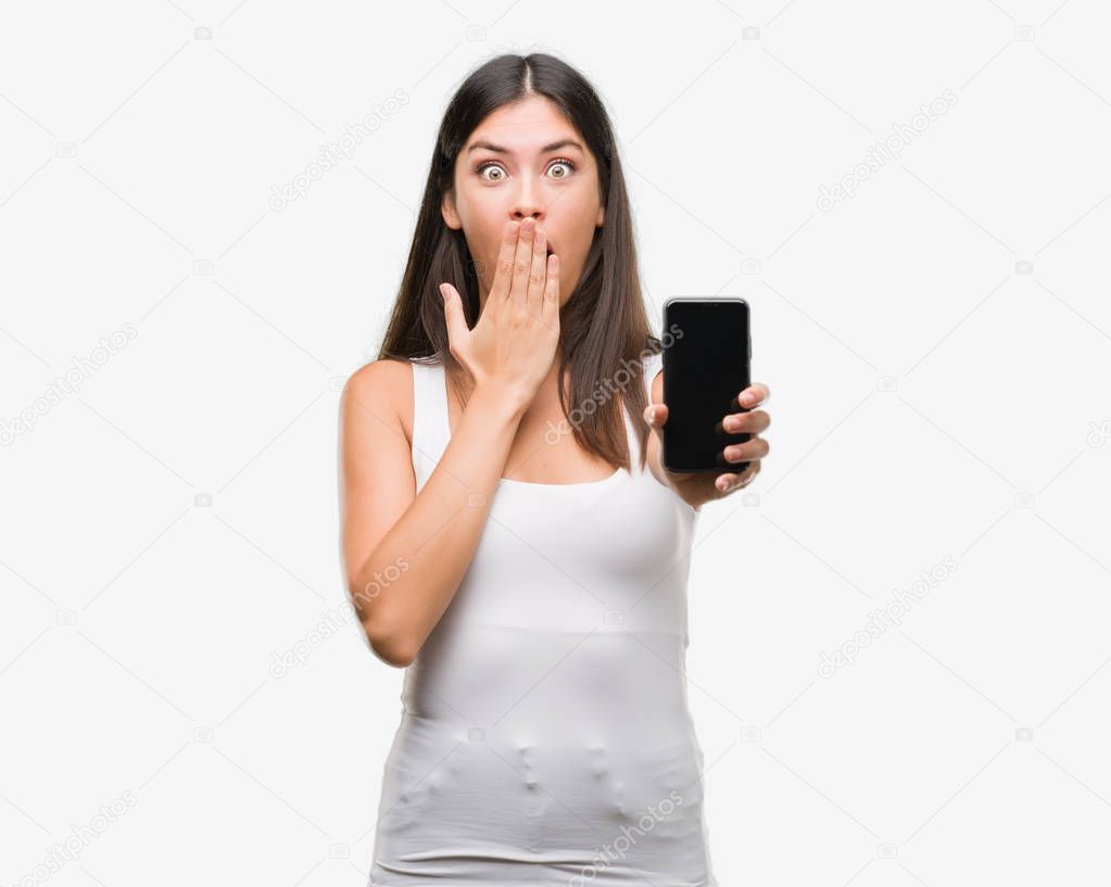 Young beautiful hispanic showing smartphone cover mouth with hand shocked with shame for mistake, expression of fear, scared in silence, secret concept