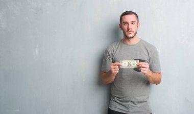 Bir dolar kendine güvenen bir ifade ile acımak yüz ciddi düşünme gösterilen gri grunge duvarın üzerinden beyaz delikanlı