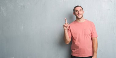 Gösterilen ve parmak gülümseyen süre bir numara ile kendinden emin ve mutlu yukarıyı gri grunge duvarın üzerinden beyaz delikanlı.