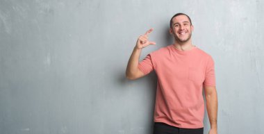 Beyaz delikanlı duvar gri grunge gülümseyen ve süre seyir ve kamera boyutu işaret parmaklarıyla yapıyor el ile kendinden emin eller üzerinde. Ölçü kavramı.