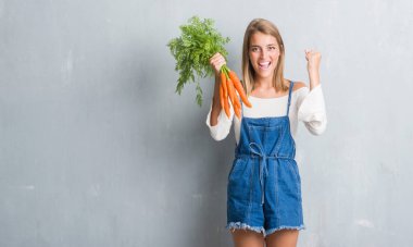 Güzel ve genç birbayan gurur çığlık ve zafer ve başarı çok heyecanlı, kutluyor taze havuç tutan grunge gri duvarın üzerinden duygu tezahürat