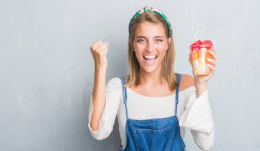 Güzel ve genç birbayan gurur çığlık ve zafer ve başarı çok heyecanlı, kutluyor meyve yeme grunge gri duvarın üzerinden duygu tezahürat