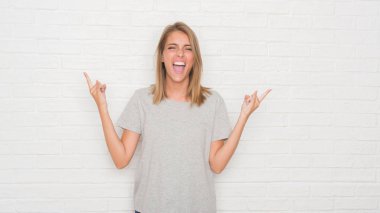 Güzel genç kadın deli ifade rock simge elle yapıyor ile bağırarak beyaz tuğla duvarın üzerinden. Müzik yıldızı. Ağır kavramı.