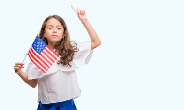 Esmer Latin kız holding Amerika Birleşik Devletleri bayrağı bir fikir ya da soru işaret parmağı gülen yüz, bir numara ile şaşırttı