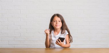 Duygu tezahürat gurur çığlık ve zafer ve başarı çok heyecanlı, kutluyor smartphone kullanarak masada oturan genç İspanyol çocuk