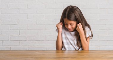 Gülümseyen ve başarı için çığlık evde çok mutlu ve heyecanlı kaldırdı, silah ile kazanan jest yapıyor masada oturan genç İspanyol çocuk. Kutlama kavramı.