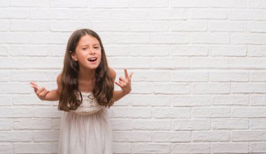 Genç İspanyol çocuk deli ifade rock simge elle yapıyor ile bağırarak beyaz tuğla duvarın üzerinden. Müzik yıldızı. Ağır kavramı.