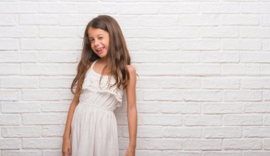 Seksi bir ifadeyle, neşeli ve mutlu yüzünü kameraya bakarak göz kırpıyor beyaz tuğla duvarın üzerinden genç İspanyol çocuk.