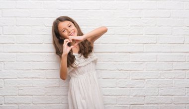 Genç İspanyol çocuğun kalp simgesi ve elleriyle şekil gösterilen aşık gülümseyen beyaz tuğla duvarın üzerinden. Romantik kavramı.