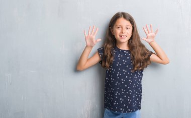 Gösterilen ve parmakları ile işaret grunge gri duvarın üzerinden genç İspanyol çocuğun kendinden emin ve mutlu gülümseyerek süre on numara.