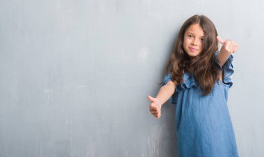 Grunge gri duvar onaylama üzerinde genç İspanyol çocuğun el ile pozitif jest yapıyor gülümseyen ve başarı için mutlu yaşasın. Kamera, kazanan jest arıyorsunuz.