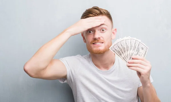 Young Redhead Man Grey Grunge Wall Holding Dollars Stressed Hand — Stock Photo, Image