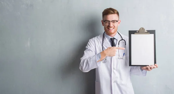 Jovem Médico Ruiva Homem Sobre Parede Grunge Cinza Segurando Prancheta — Fotografia de Stock