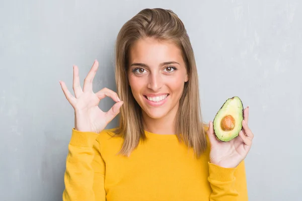 Beautiful Young Woman Grunge Grey Wall Eating Avocado Doing Sign — Stock Photo, Image