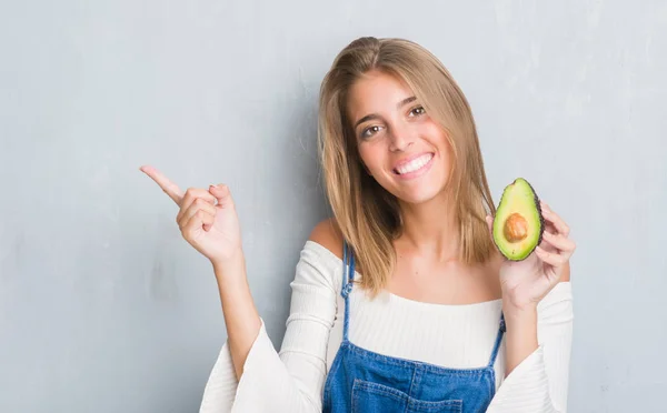 Hermosa Mujer Joven Sobre Pared Gris Grunge Comiendo Aguacate Muy —  Fotos de Stock