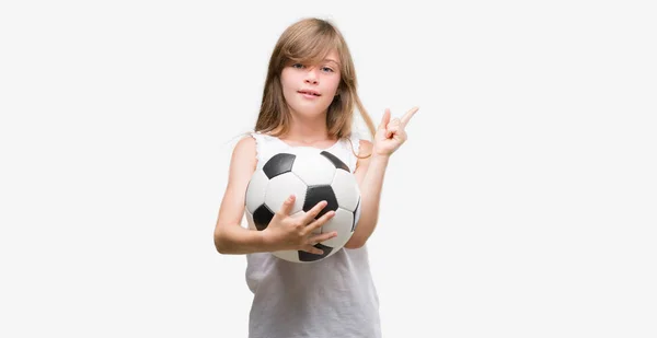 Молодой Блондин Держащий Футбольный Мяч Счастлив Указывая Рукой Пальцем Сторону — стоковое фото