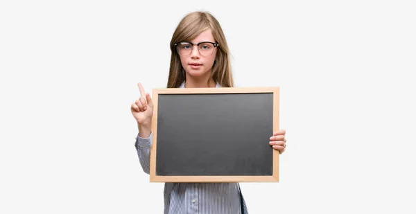 Young Blonde Child Holding Blackboard Surprised Idea Question Pointing Finger — Stock Photo, Image