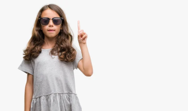 黑发西班牙裔女孩戴着太阳镜显示和指着手指第一 而微笑着自信和快乐 — 图库照片