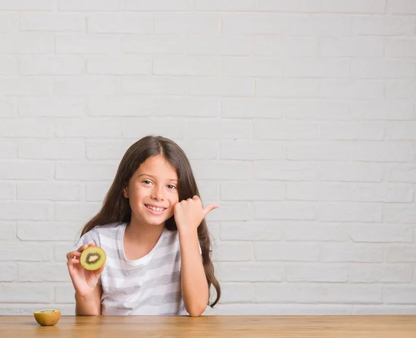Młode Dziecko Hiszpanin Siedzi Stole Jedzenie Kiwi Wskazując Wyświetlono Kciukiem — Zdjęcie stockowe
