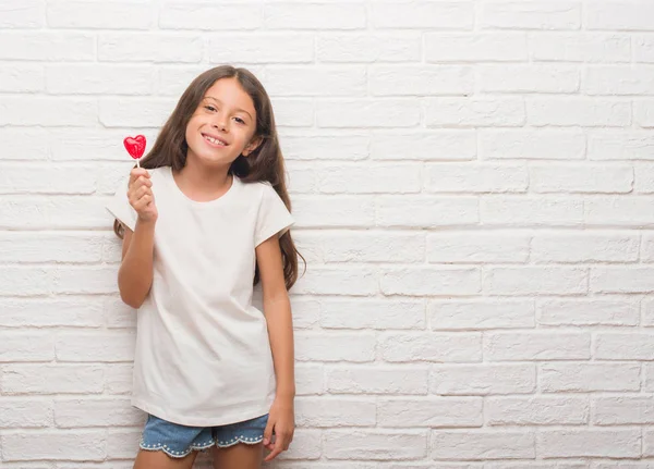 Junges Hispanisches Kind Über Weißer Ziegelwand Das Rote Herzlutscher Bonbons — Stockfoto