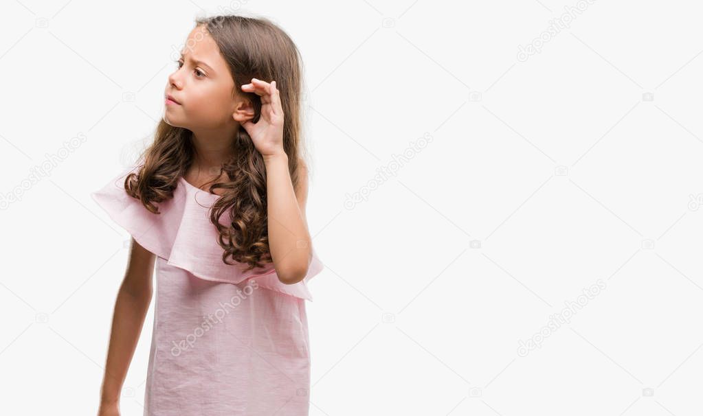 Brunette hispanic girl wearing pink dress smiling with hand over ear listening an hearing to rumor or gossip. Deafness concept.