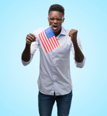 Genç Afrikalı-Amerikalı adam holding ABD bayrağı rahatsız ve boşa çıkarmak ile öfke, çılgın ve yükseltilmiş eliyle diye bağıran öfke kavramı bağırarak.