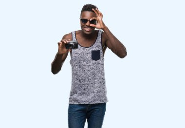 Vintage fotoğraf makinesi ile ok işareti ile el parmaklarının arasından seyir göze yapıyor gülümseyen mutlu yüz tutan genç Afro-Amerikan adam