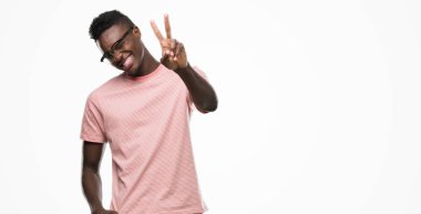 Pembe tişört gülümseyen zafer işareti yapıyor parmak gösterilen kamera seyir giyen genç Afro-Amerikan adam. İki numaralı.