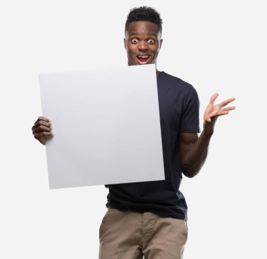 Kocaman bir gülümseme ile çığlık ve ellerini kaldırdı zaferini kutluyor bir afiş çok mutlu ve heyecanlı, kazanan ifade tutan genç Afro-Amerikan adam