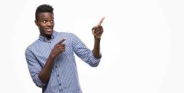 Genç Afro-Amerikan adam mavi tişört giyiyor gülümseyen ve iki elleri ve parmakları ile tarafına işaret kamera bakıyor.