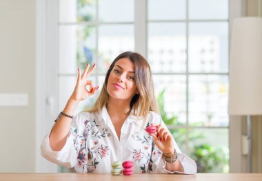 Genç kadının evde parmak, mükemmel sembolü ile ok işareti yapıyor macarons yediğini