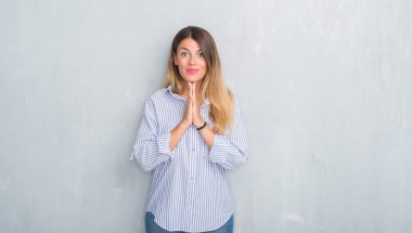 Genç Yetişkin kadın moda iş kıyafeti ellerle birlikte AF emin gülümseyen için soran dua giyen gri grunge duvarın üzerinden.